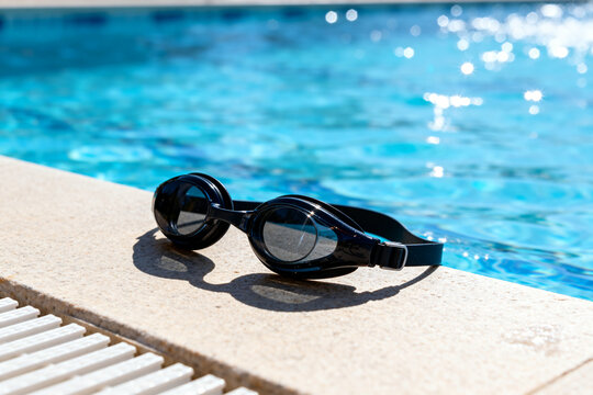 Black swimming goggles resting on pool edge with sparkling water background