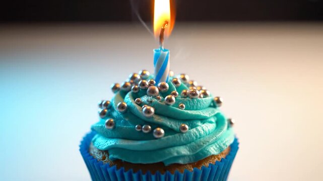 Blue birthday cupcake with silver sprinkles and a single lit candle on a blurred background