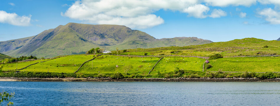 Green mountain slopes rise above Killary Fjord under bright skies in western Ireland. This image is a scenic landscape focused more on the fjord lush hillsides than the water.