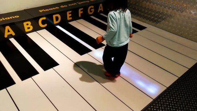 A cute little girl is playing a giant piano by stepping on it.