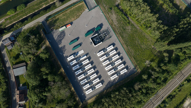 Aerial view of the Elia TS Ville sur Haine battery energy storage system with rows of white units surrounded by lush green trees in Mons, Region wallonne, Belgium.