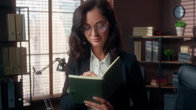 Glad Caucasian business woman wearing glasses writing notes in office female businesswoman holding pen planning finance tasks notebook project planner worker manager education teacher studying indoors