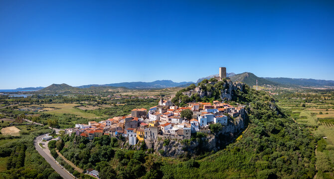 Aerial view of the historic hilltop town of Posada featuring the Castello della Fava tower, colorful houses, and lush green surroundings in Posada, Sardinia, Italy.