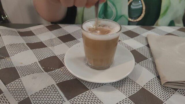 Woman stirring frothy coffee with cinnamon in cafe