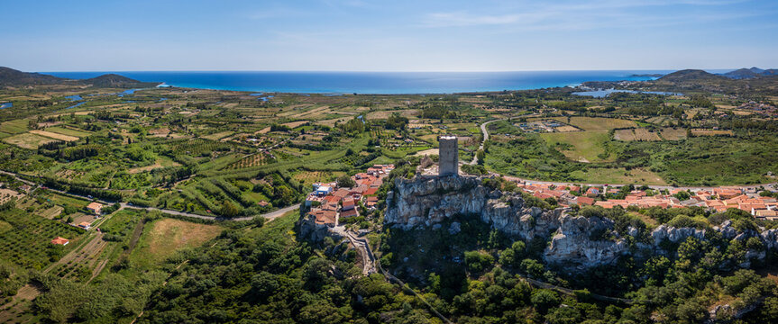 Aerial view of the historic Castello della Fava perched on a rocky hill overlooking the town and the Mediterranean Sea under a clear blue sky in Posada, Sardinia, Italy.