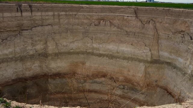 Ground-level footage showing a large sinkhole with steep eroded walls in a rural landscape. Geological formation, natural ground collapse, karst terrain, and dry soil textures are clearly visible.