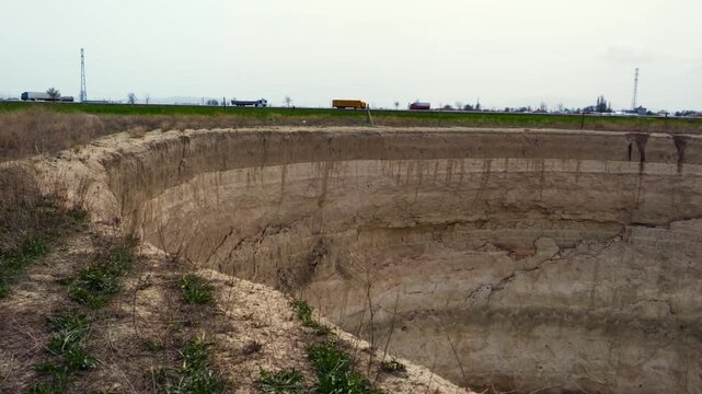Ground-level footage showing a large sinkhole with steep eroded walls in a rural landscape. Geological formation, natural ground collapse, karst terrain, and dry soil textures are clearly visible.