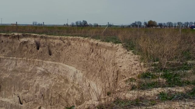 Ground-level footage showing a large sinkhole with steep eroded walls in a rural landscape. Geological formation, natural ground collapse, karst terrain, and dry soil textures are clearly visible.