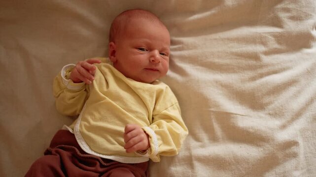 Expressive newborn baby lying on a bed, moving and making a range of emotional faces, from wide eyed curiosity and yawning to fussing, crying, and showing signs of discomfort