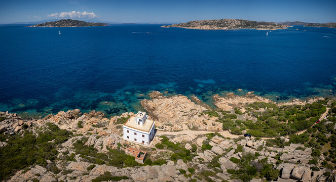 Aerial view of Faro di Punta Sardegna lighthouse overlooking the turquoise sea and rocky coastline in Palau, Sardegna, Italy.