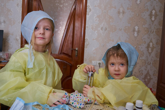 Two little girls play doctors in medical gowns and caps, girlfriends at home play hospital, Concept of children's imagination, role-playing games, future profession of a doctor or nurse.