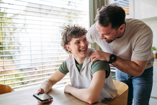 Father supporting teenage son at home during everyday moment.