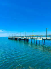 Obraz premium View of a long pier extending into clear blue water on a sunny day with bright sky and few clouds