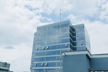 Fototapeta premium Building stands tall against cloudy sky with blue glass reflecting light in urban area during afternoon