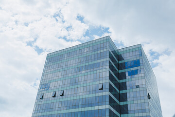 Naklejka premium Tall office building with glass windows under cloudy sky in a city during daytime near the end of summer