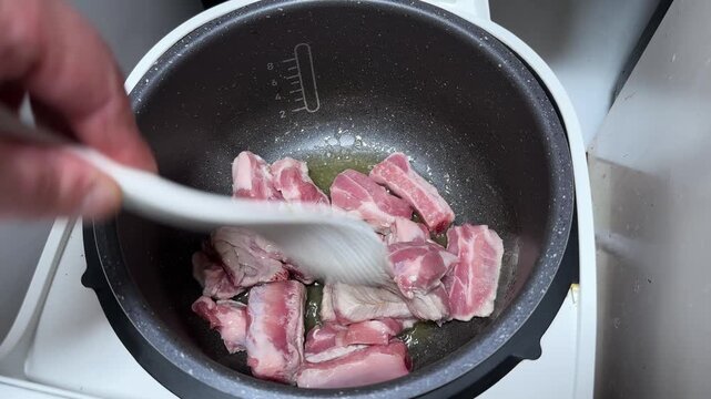 Stirring pork ribs in multi-cooker pot with melted fat