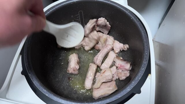 Stirring pork ribs in multi-cooker pot during frying