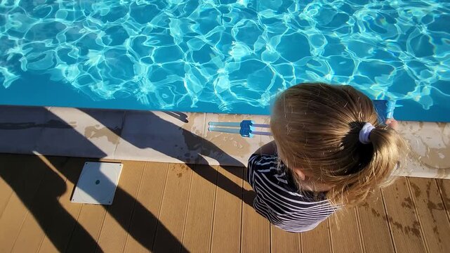 High-angle view of a toddler girl looking at a pool tool on the deck