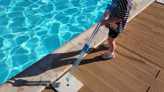Toddler girl standing on a wooden deck with a long pool skimmer pole