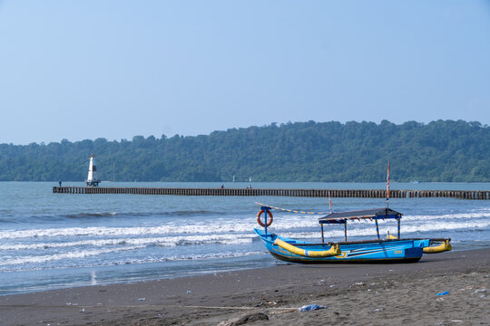 Cilacap, Indonesia - May 13, 2026: Scenic view of Teluk Penyu Beach with traditional fishing boats on the black sand and Nusakambangan island in the background.
