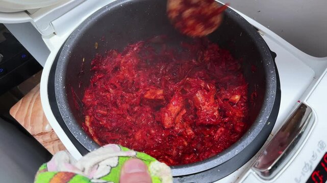 Stirring vegetables and pork with tomato sauce in multi-cooker