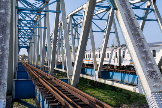 Kebumen, Indonesia - May 14, 2026: KAI train crossing the historical Renville steel truss bridge over parallel railway tracks on a sunny day.