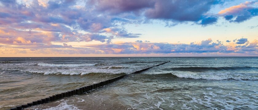 Panoramic sunset over the Baltic Sea with a traditional wooden groin in the waves - real photography - authentic - no ai
