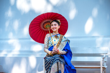 Obraz premium Beautiful Thai woman in Thai traditional dress holding red umbrella in Thai temple