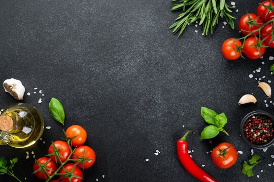 Fresh tomatoes, basil, rosemary, spices and olive oil bottle on black table.