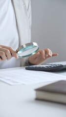 Fototapeta premium Businesswoman carefully reviewing financial reports using magnifying glass and calculator, close up vertical view. Audit and taxes in business