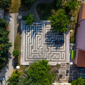 Aerial view of a square paved with a labyrinth pattern surrounded by green trees and urban buildings in Tirana, Tirana County, Albania.