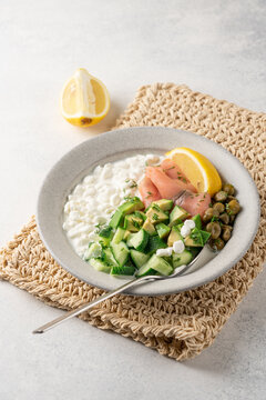 Fresh high protein savory cottage cheese bowl with smoked salmon, avocado, cucumber, capers and dill served on light background with copy space