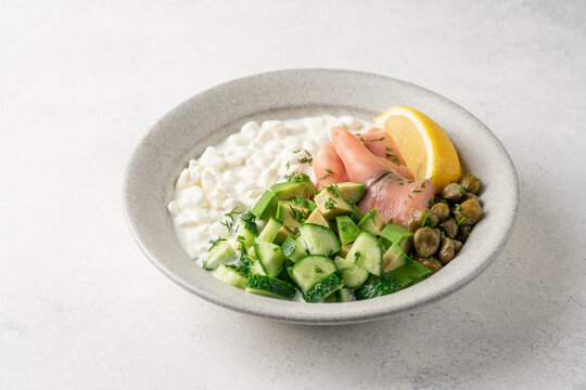 Fresh high protein savory cottage cheese bowl with smoked salmon, avocado, cucumber, capers and dill served on light background with copy space