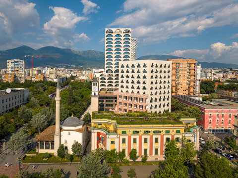 Aerial view of the Et'hem Bey Mosque and Clock Tower of Tirana surrounded by modern skyscrapers and green trees under a cloudy sky in Tirane, Tirana County, Albania.