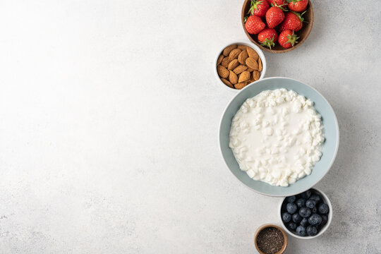 Fresh ingredients for a high protein cottage cheese bowl including blueberries, strawberries, chia seeds and almonds arranged on a light background with copy space