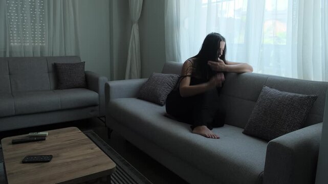 Woman experiencing auditory hallucinations while sitting alone on sofa, hearing voices and struggling with psychological distress and mental health challenges