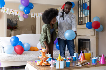 Obraz premium Couple standing at coffee table arranging balloons and cupcakes with green overshirt, checked shirt