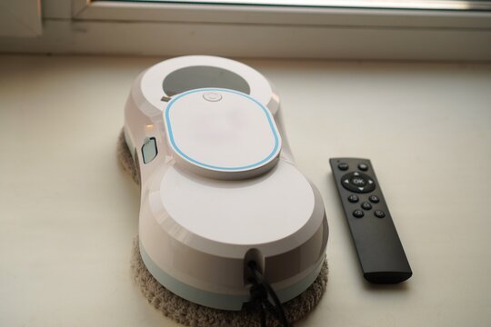Window cleaning robot on a surface beside a remote control. The device is designed for efficient cleaning, simplifying household chores through automation and user-friendly technology