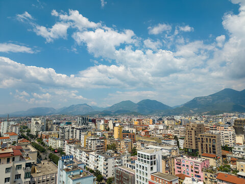 Aerial view of the urban skyline with colorful apartment buildings and distant mountains under a bright blue sky with fluffy clouds Tirane, Tirana County, Albania.