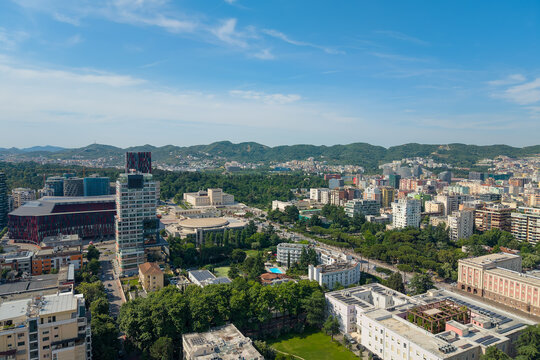 Aerial view of modern skyscrapers, the national stadium, and lush green parks under a clear blue sky in the city center Tirane, Tirana County, Albania.