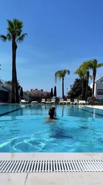back view of woman swimming in luxury resort pool, authentic summer vacation lifestyle