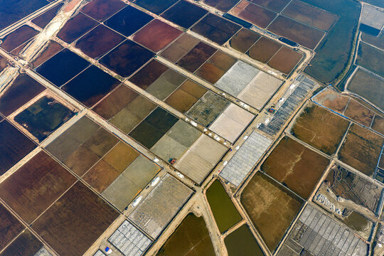 Aerial view of the geometric grid of colorful salt evaporation ponds and dirt paths in Dong Hai, Ninh Thuan, Vietnam.
