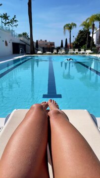 pov of woman legs on sun lounger with man swimming laps in resort pool, authentic summer vacation lifestyle