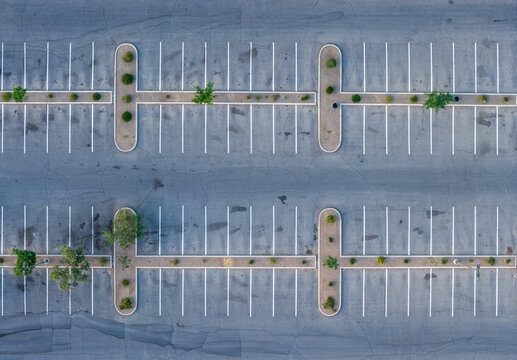 Aerial view of an empty asphalt parking lot with white painted lines and landscaped islands featuring small green trees and shrubs in Summerlin South, Nevada, United States.