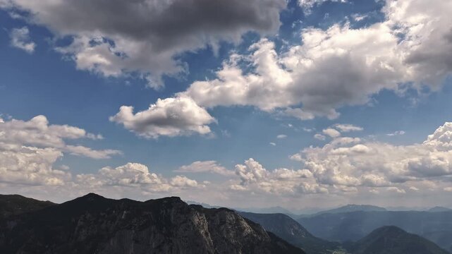 Hyperlapse footage of dramatic clouds moving over the Austrian Alps with mountain ridges, blue sky, sunlight and atmospheric landscape. Ideal for travel, nature, tourism and outdoor projects.
