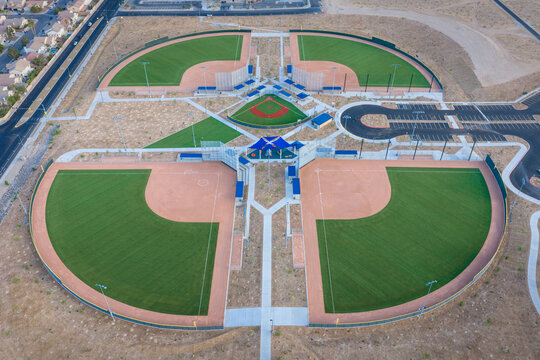 Aerial view of a modern baseball complex featuring multiple green turf diamonds and dirt infields under soft daylight Summerlin South, Nevada, United States.