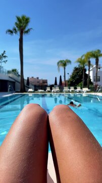 point of view of woman legs sunbathing by a luxury resort swimming pool, authentic summer vacation lifestyle