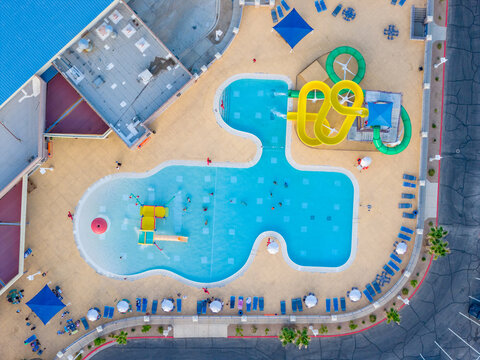 Aerial view of a vibrant water park featuring a large swimming pool, colorful water slides, and people relaxing under umbrellas in Summerlin South, Nevada, United States.