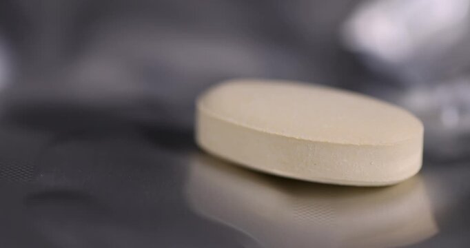 A yellow oval tablet on a blister, this medicinal tablet lies on a silver foil package next to the convex cells.