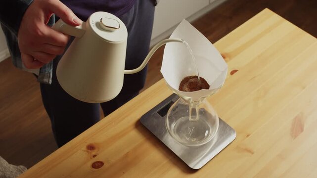 Man brewing coffee in glass dripper with blooming stage on kitchen scale
